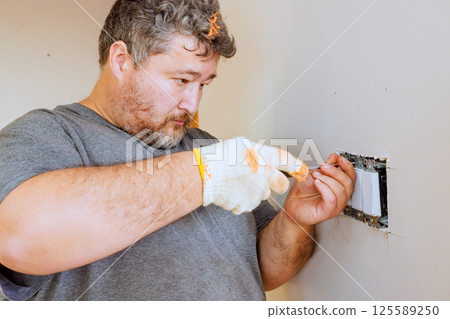 Electrician working on fixing wall switch while renovating room in residential space. 125589250