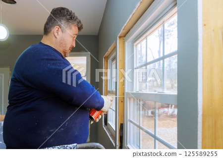 Worker is applying insulation sealant foam around windows while renovating house interior setting. 125589255