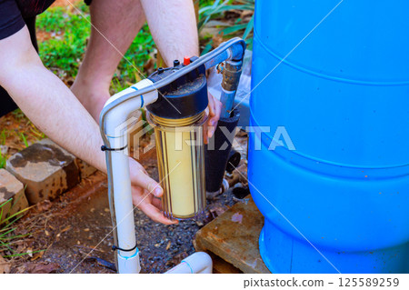 Person is changing yellow filter in water filtration system in backyard 125589259