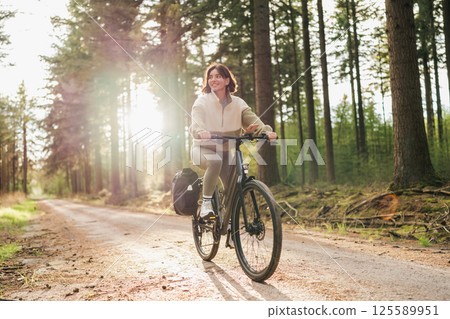 Wellness in motion, a vibrant woman pedals her way through a peaceful forest retreat at sunset Wellness in motion, a vibrant woman pedals her way through a peaceful forest retreat at sunset 125589951