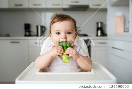 Cute caucasian baby eating broccoli in high chair at home kitchen. concept of healthy eating, child nutrition, early development 125590003