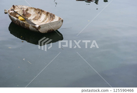 a weathered aged rowboat floating gently on calm water, cracked and peeling paint, with reflection on the water. There is copyspace. 125590466