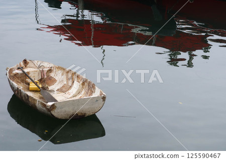 a weathered aged rowboat floating gently on calm water, cracked and peeling paint, with reflection on the water. There is copyspace. 125590467