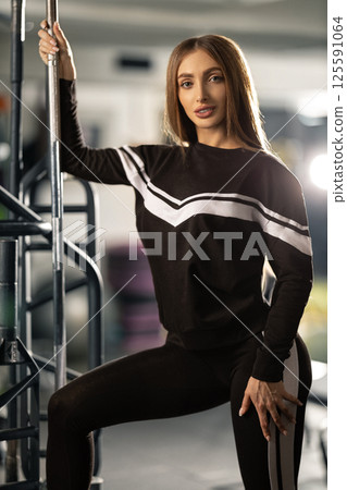 fitness enthusiast is striking dynamic pose while holding onto gym equipment. setting features sleek workout machines and atmosphere is energized and motivational. 125591064