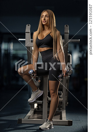 fitness enthusiast showcases strength and determination while holding dumbbells in gym. workout session takes place in evening highlighting commitment health. 125591087