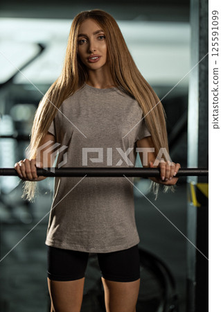 young athlete long hair prepares for strength training session in well equipped gym. She demonstrates focus while gripping barbell showcasing determination. young athlete long hair prepares for strength training session in well equipped gym. She demonstrates focus while gripping barbell showcasing determination. 125591099
