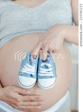 Tender Pregnancy Moment: Baby Shoes Resting on Expectant Mother's Belly Tender Pregnancy Moment: Baby Shoes Resting on Expectant Mother's Belly 125591215