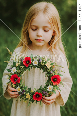 Beautiful summer wreath of field flowers in the hands of a little blond girl. Summer spring time. Background of the summer solstice. The festival of Ivan Kupala. 125591407