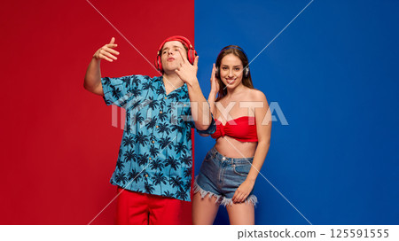 Man in headphones gesturing, dancing, woman smiling calm, expressing rhythm and fun against split red and blue background. 125591555