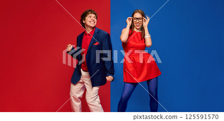 Happy young man and woman in dress and costume, cheerfully dancing against split red and blue background 125591570