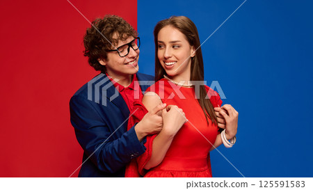 Portrait of happy, loving couple, hugging and smiling with warmth and connection against red and blue background. 125591583