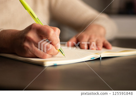 Warm toned image of hand writing personal thoughts in diary. Blurred background for cozy atmosphere. 125591848