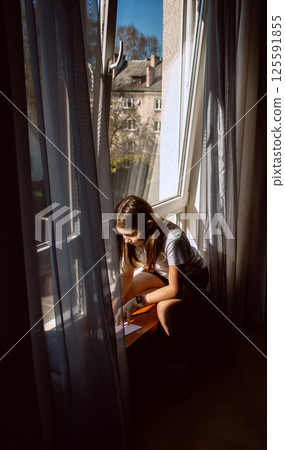 Preteen girl drawing something while sitting on windowsill. Self-expression through art. Image for creative play and children cognitive development in concept. 125591855