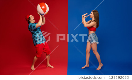 Man tossing beach ball to laughing woman in playful interaction with carefree beach attitude against red and blue background. 125592033