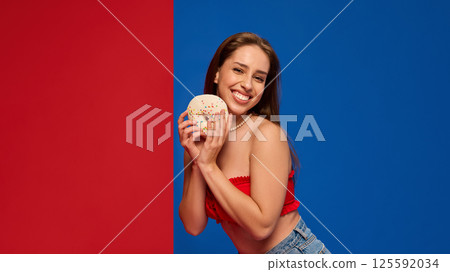 Smiling woman holding donut playfully in colorful scene 125592034