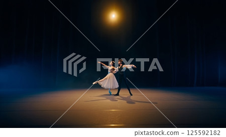 A male and female ballet dancer in mid-pirouette on a grand theater stage, bathed in a golden spotlight A male and female ballet dancer in mid-pirouette on a grand theater stage, bathed in a golden spotlight 125592182
