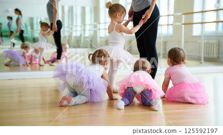A chaotic yet adorable scene of toddlers in tiny tutus and leggings attempting plies in a mirrored studio A chaotic yet adorable scene of toddlers in tiny tutus and leggings attempting plies in a mirrored studio 125592197