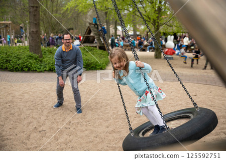 Father rolls daughter on a swing at the playground 125592751