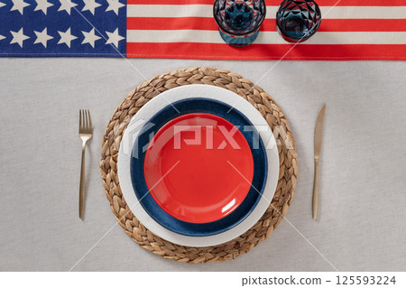 Patriotic table setting for USA Independence Day. Festive dinner with empty red plate and decoration in USA national flag colors white, red and blue. View from above. Copy space. Patriotic table setting for USA Independence Day. Festive dinner with empty red plate and decoration in USA national flag colors white, red and blue. View from above. Copy space. 125593224