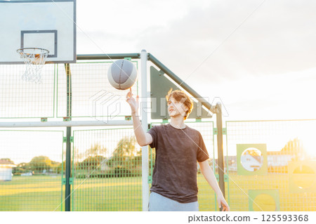 Young male skillfully spinning a basketball at a sunny outdoor court. Playing Basketball at Park outdoor playground in sunset light. Basketball match. Teenagers' hobby. Sports and healthy lifestyle 125593368