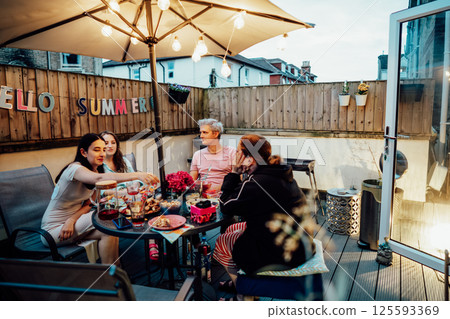 Friends enjoying summer evening on private outdoor patio terrace with drinks and snacks. Friends dining, drinking cocktails, having fun together on patio party event. Millennials lifestyle concept. Friends enjoying summer evening on private outdoor patio terrace with drinks and snacks. Friends dining, drinking cocktails, having fun together on patio party event. Millennials lifestyle concept. 125593369