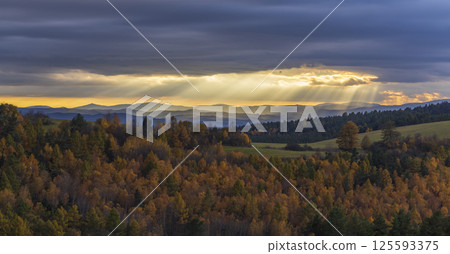 Sun rays shining through clouds over colorful autumn forest landscape with Low Tatras Sun rays shining through clouds over colorful autumn forest landscape with Low Tatras 125593375