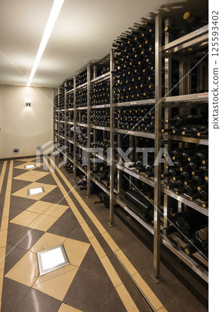 Wine bottles aging on metal shelves in cellar with tiled floor 125593402