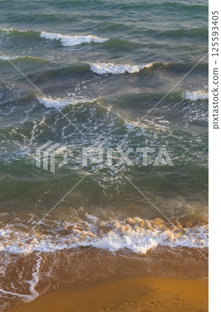 Gentle waves washing golden sandy beach at sunset 125593405