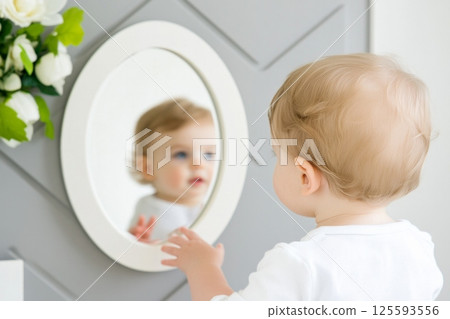 Curious toddler exploring their reflection in a modern nursery with soothing decor for the first time 125593556