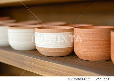 Close-up view of handmade pottery bowls in natural clay tones on a dark wooden shelf with warm lighting Close-up view of handmade pottery bowls in natural clay tones on a dark wooden shelf with warm lighting 125593612