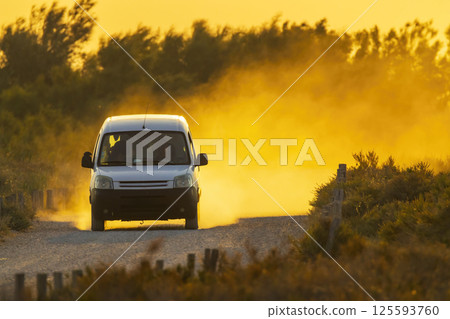 White van driving on dusty road at sunset White van driving on dusty road at sunset 125593760