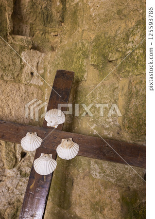 Wooden cross decorated with seashells hanging on ancient stone wall 125593786