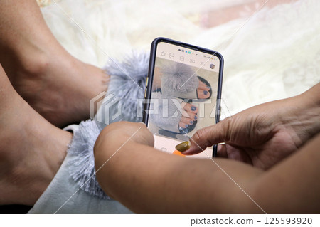 A manicurist is taking a photo of his painted toenails with his cell phone. A manicurist is taking a photo of his painted toenails with his cell phone. 125593920