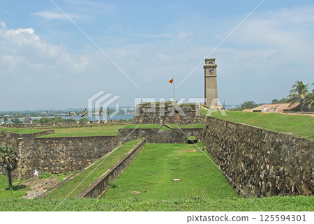 Galle Clock Tower and Flag with Visitors Relaxing Nearby, Galle, Sri Lanka 125594301