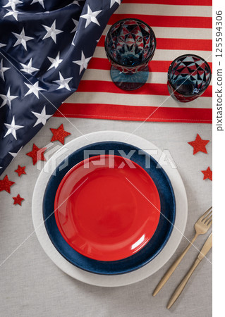 Table setting for USA Independence Day. Festive dinner with empty red plate and decoration in USA national flag colors and stars. Copy space. Vertical. View from above 125594306