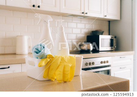Kitchen cleaning supplies on countertop with gloves and spray bottles in modern white interior 125594913