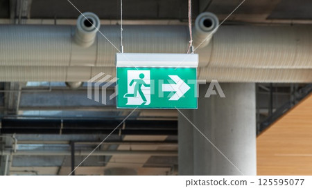 Exit sign with a right-pointing arrow, hanging from the ceiling, guiding the way out for emergency evacuation. A universal safety symbol in buildings. Exit sign with a right-pointing arrow, hanging from the ceiling, guiding the way out for emergency evacuation. A universal safety symbol in buildings. 125595077