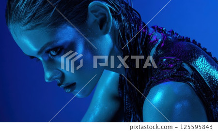 A model with wet hair and striking features is captured in dramatic blue lighting, emphasizing her intense expression and unique outfit during a creative studio photoshoot 125595843