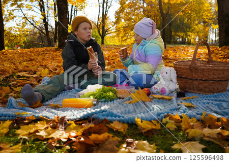 Boy and girl enjoying having picnic together in public park on sunny autumn day 125596498