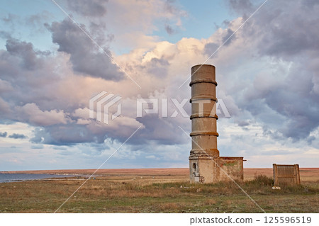 Concrete lighthouse tower in the steppe against a landscape with clouds Concrete lighthouse tower in the steppe against a landscape with clouds 125596519