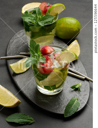 Refreshing mojito cocktail with lime, mint, strawberry, and ice on dark background Refreshing mojito cocktail with lime, mint, strawberry, and ice on dark background 125596644
