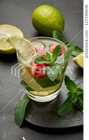 Refreshing mojito cocktail with lime, mint, strawberry, and ice on dark background Refreshing mojito cocktail with lime, mint, strawberry, and ice on dark background 125596646