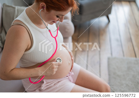 A pregnant woman listens to her baby's pulse using a phonendoscope. A pregnant woman listens to her baby's pulse using a phonendoscope. 125596772