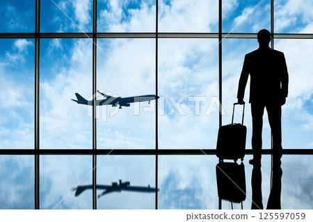 Business traveler waiting at the airport as a plane flies in the distance during daytime 125597059