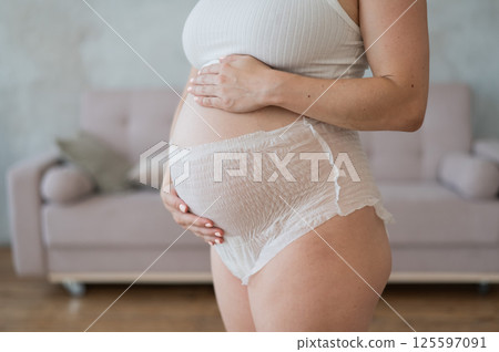 Caucasian pregnant woman in adult diapers suffers from incontinence. Close-up of belly.  125597091