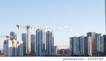 A panoramic view of urban construction with cranes and tall highrises set against a bright blue sky 125597107