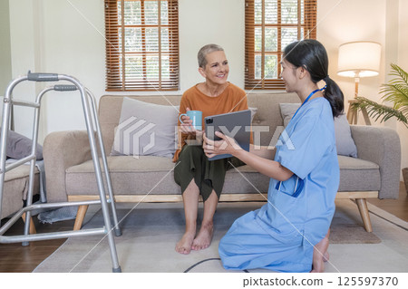 Young Nurse Offering Health Care Advice to Elderly Woman in a Cozy Living Room Setting Young Nurse Offering Health Care Advice to Elderly Woman in a Cozy Living Room Setting 125597370