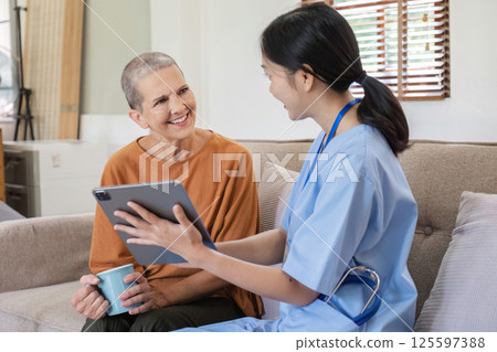 Young Nurse Providing Health Care Advice to Elderly Woman in a Comfortable Home Setting with Digital Tablet and Warm Smiles 125597388