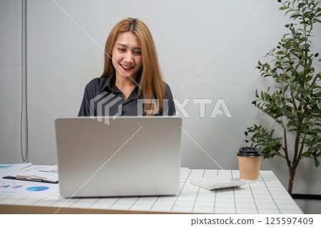 Businesswoman Analyzing Financial Graphs on Laptop in Modern Office Setting with Coffee and Documents 125597409