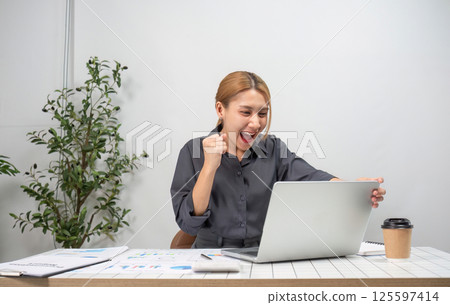 Successful Businesswoman Celebrating Achievement at Work in Modern Office Environment with Laptop and Documents Successful Businesswoman Celebrating Achievement at Work in Modern Office Environment with Laptop and Documents 125597414